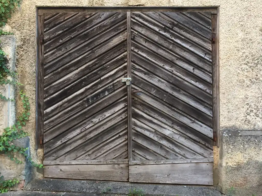 Weathered wooden swing-out garage doors set in an old plaster wall
