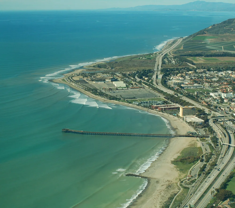 Aerial view of a coastline with a freeway, beach homes and a long breakwater